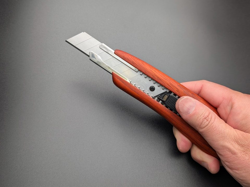 A cutter knife with a red padouk wood handle, held in a hand