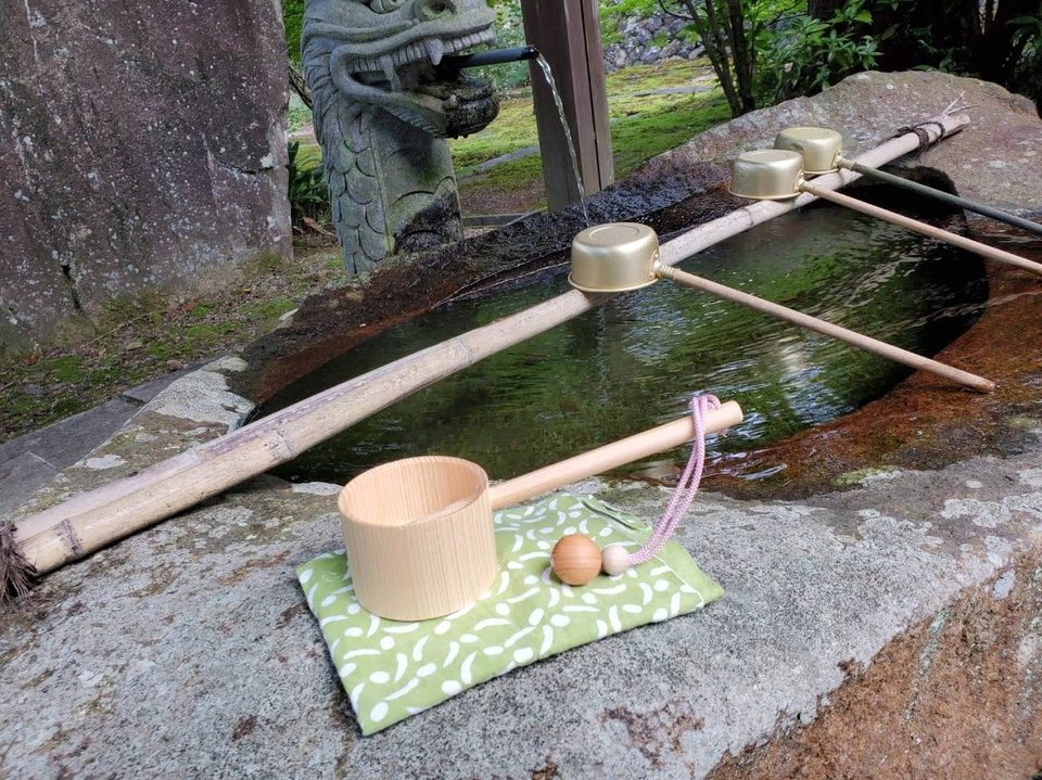 A small wooden ladle resting beside a stone water basin at a Japanese shrine